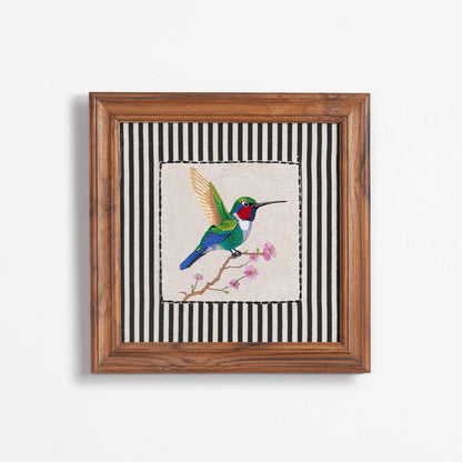 Vliving BOTANICAL hummingbird embroidered wall art with teak wood frame, featuring a colorful hummingbird on a branch with pink flowers against a black and white striped background.