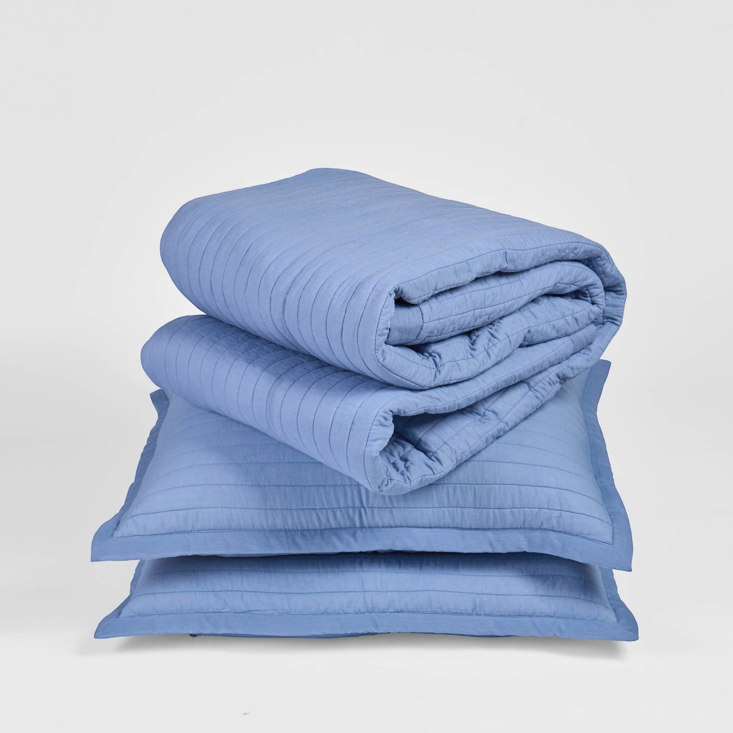 Vliving denim blue quilted cotton bedspread with stripe quilting and border, folded on top of two pillow shams.