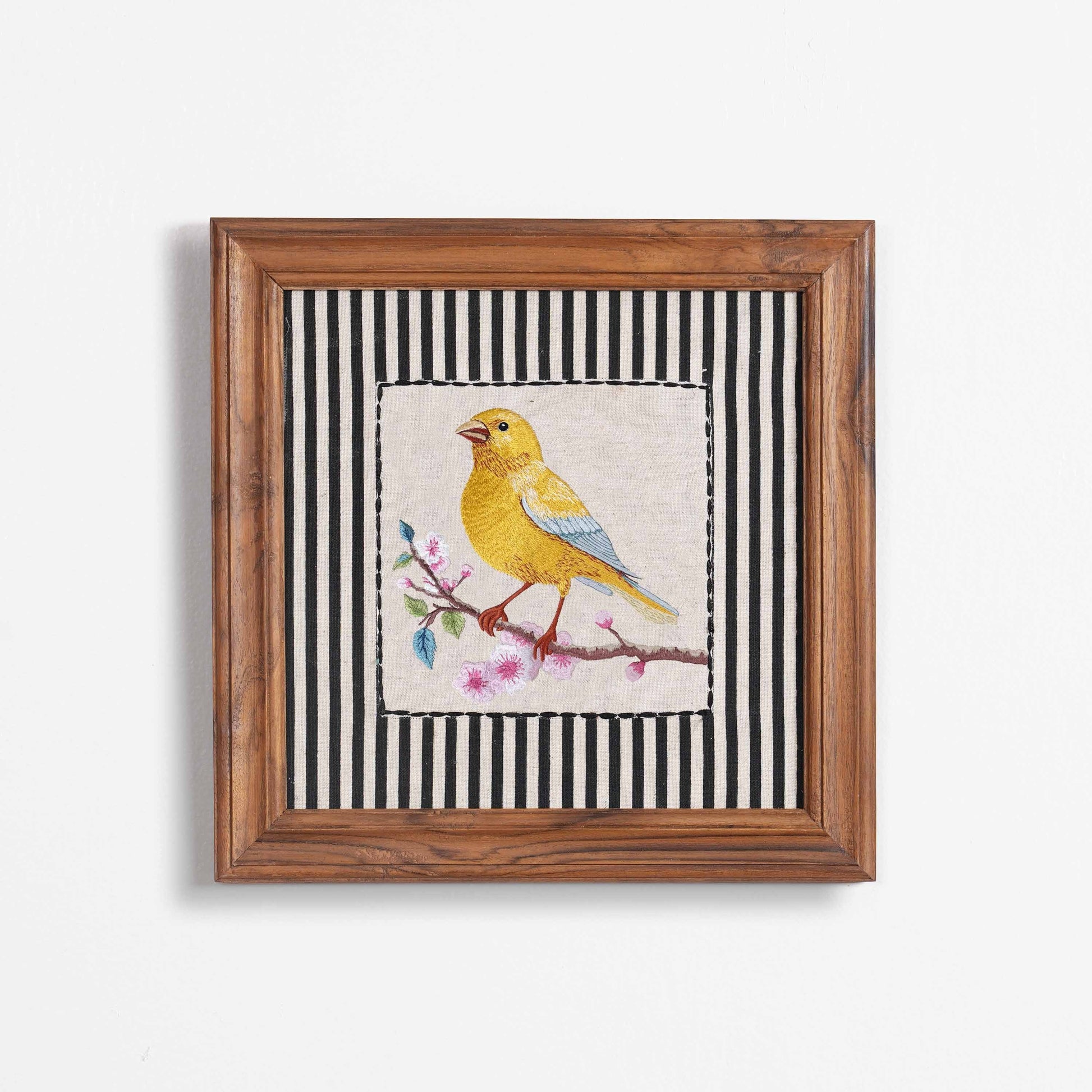 Vliving framed embroidered canary yellow bird wall art with pink blossoms on a linen fabric with black and white striped background.
