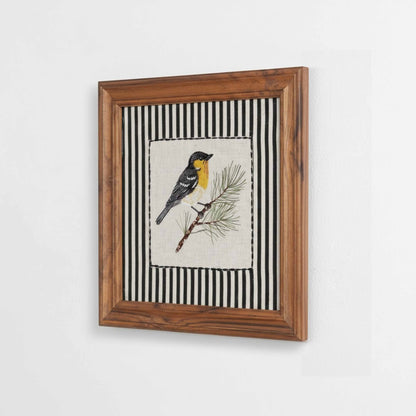 Vliving embroidered yellow and grey bird on a pine branch, framed in wood with black and white striped background.