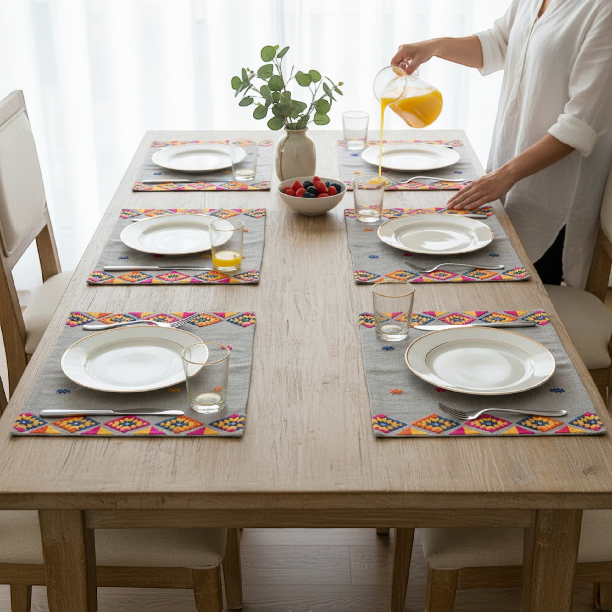Vliving grey linen table mats with multicolour kilim embroidery and gold-rimmed plates.